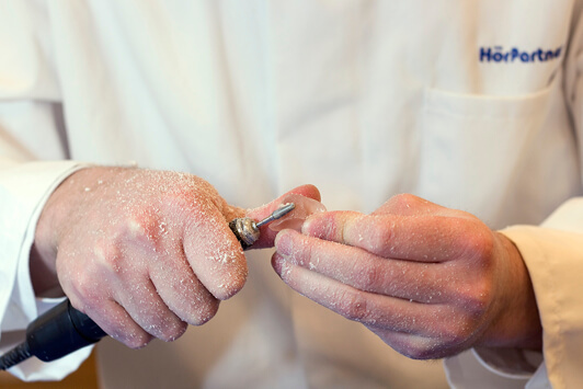 Ein Hörakustiker schleift ein Hörgerät präzise in einer Fachwerkstatt von Hand.